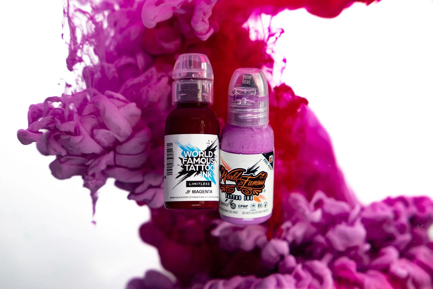 Two bottles of tattoo ink, one labeled 'World Famous Tattoo Ink' in magenta color and the other labeled 'Limitless,' placed against a colorful pink and purple marbled background.