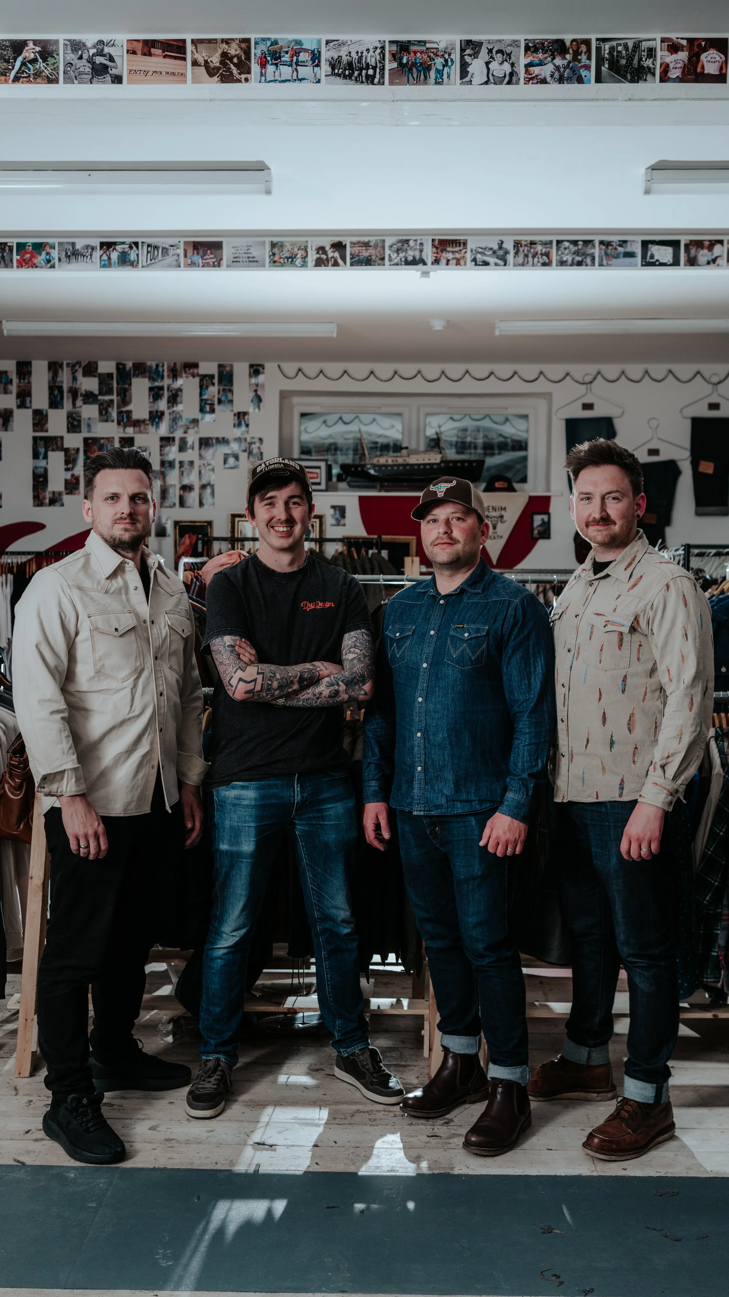 Four men standing in a row inside a clothing store, with photo displays on the wall behind them and large windows in the background.