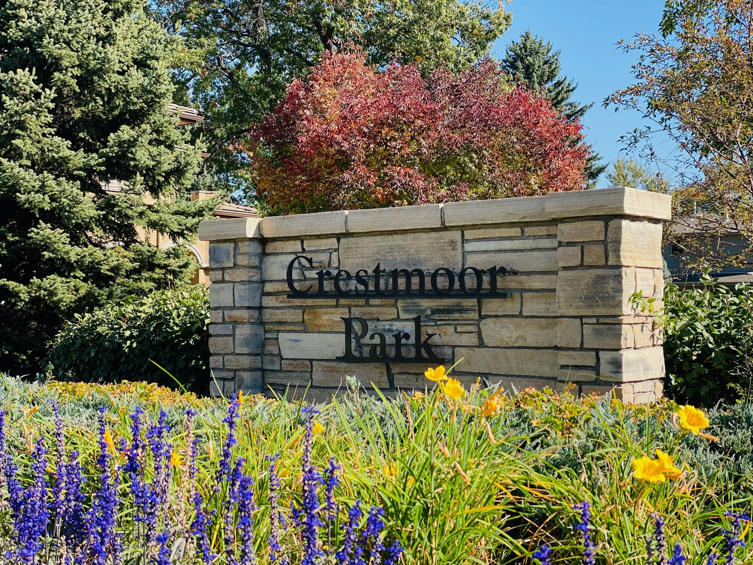 Stone sign reading 'Crestmoor Park' surrounded by colorful flowers and trees in the background.