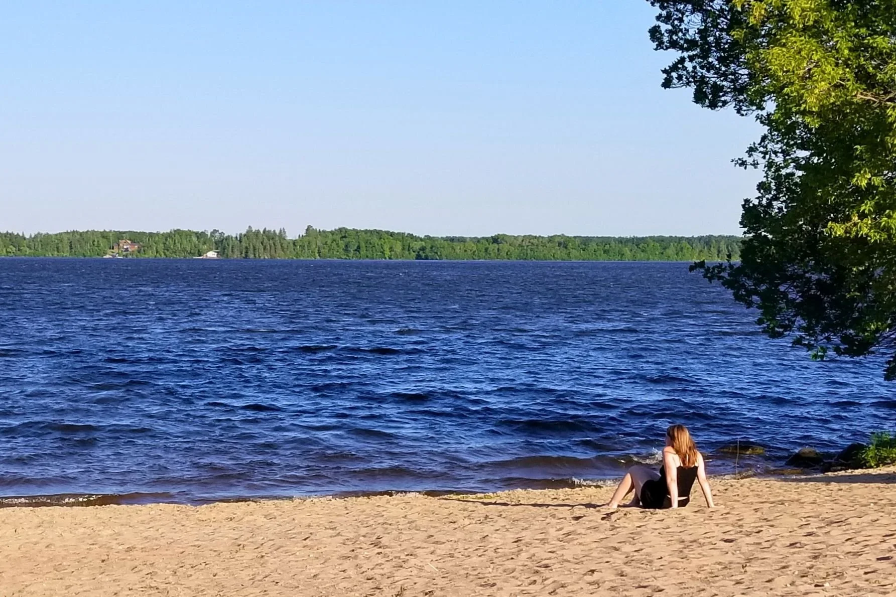 A woman sitting in the side along a Winnipeg River beach