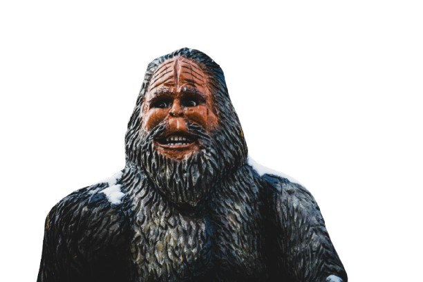 A statue of a caveman with long hair, a beard, and a cheerful expression, made of a material resembling stone or wood.