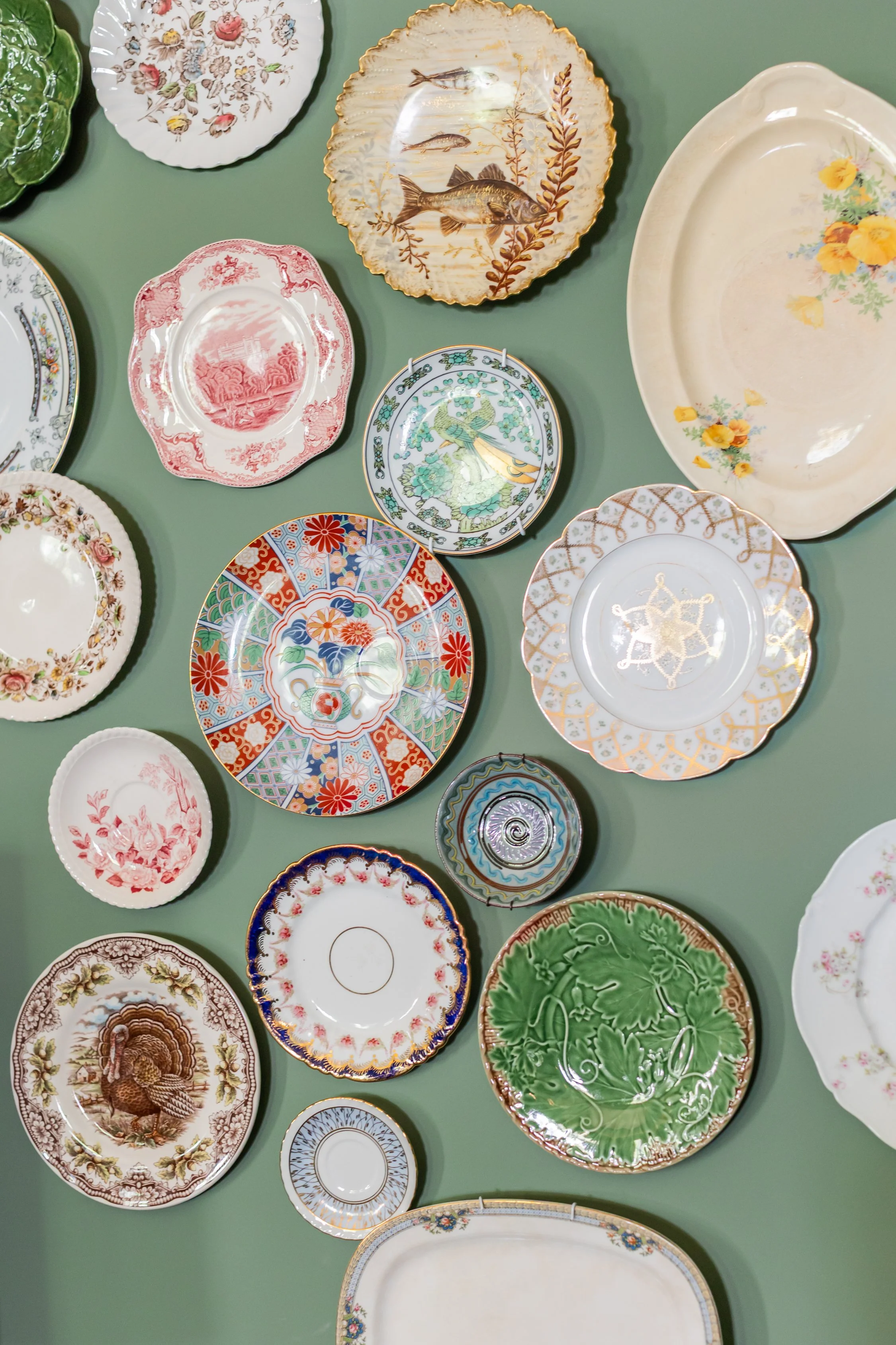 A curated plate wall composed of heirloom pieces belonging to the U-Fab Interiors design team, featured in the Living & Dining Room at the 2026 RSL Designer Show House at Foundry Manor.