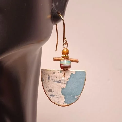 Earring with a half-moon shaped pendant, gold bead, and multicolored bead, hanging from a gold hook, displayed against a pink background.