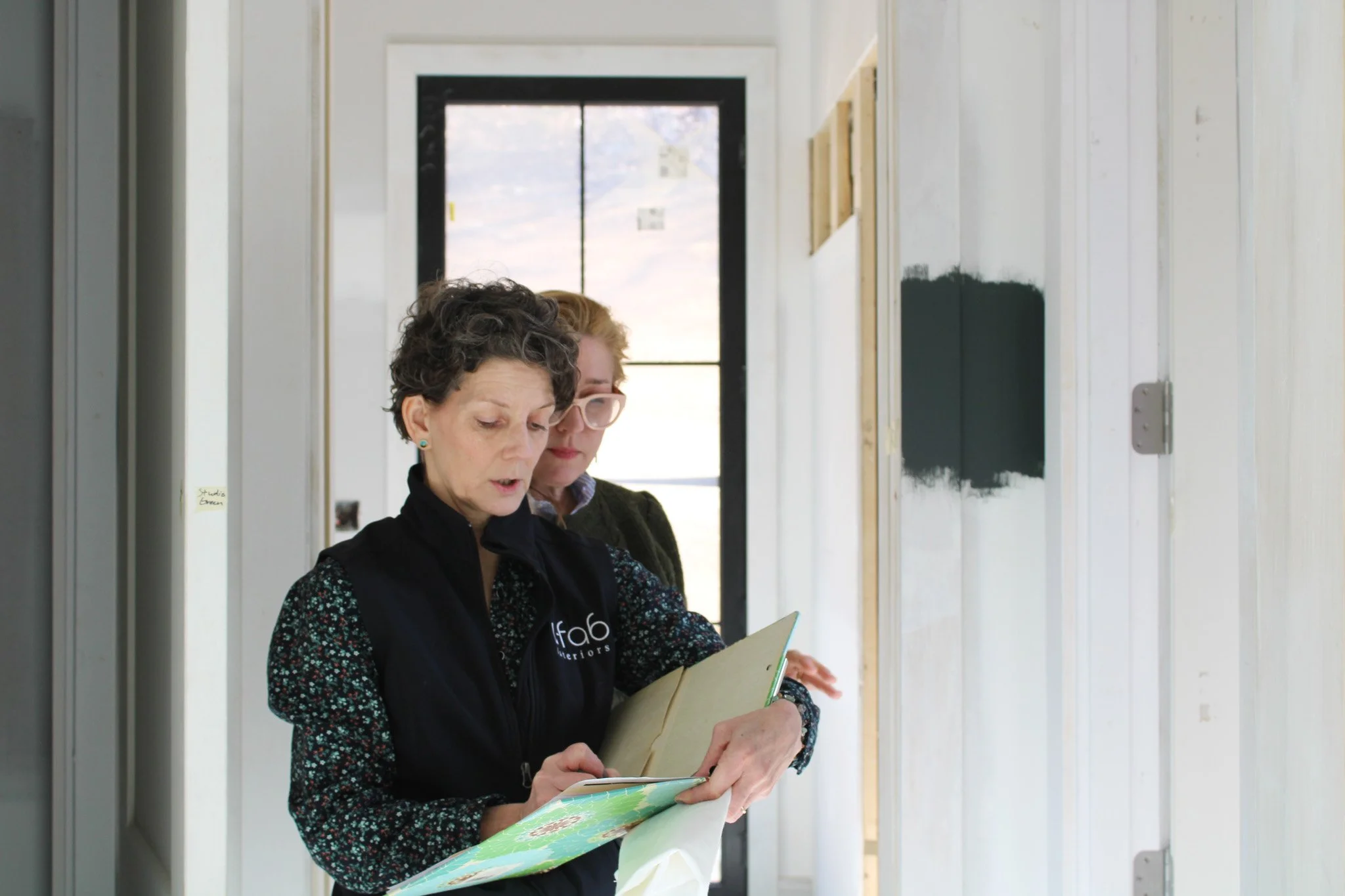 U-Fab Interiors design consultant Diana Vicenti reviews notes on a clipboard with a client during an in-home consultation, with paint color swatches displayed on the wall behind them.