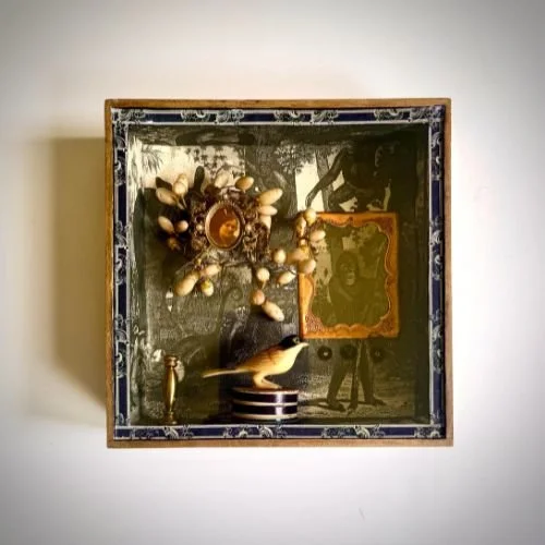 Decorative shadow box with vintage collage, bird figurine, artificial flowers, and ornate frame.