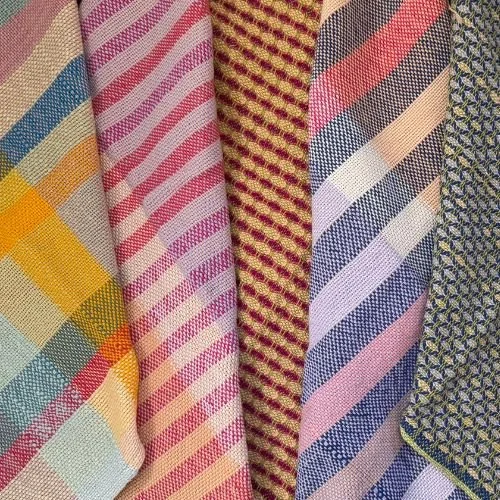 Close-up of multiple folded colorful fabric swatches with various striped and checkered patterns.