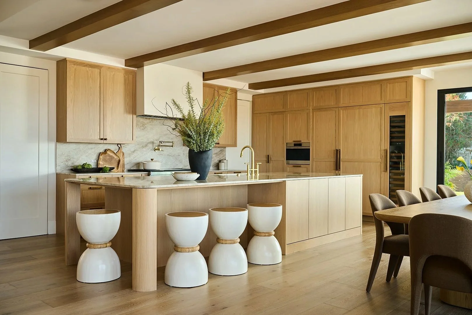 Modern living room with white sectional sofa, large flat-screen TV, and sliding glass doors leading to outdoor patio with seating and a view of the city skyline and water.