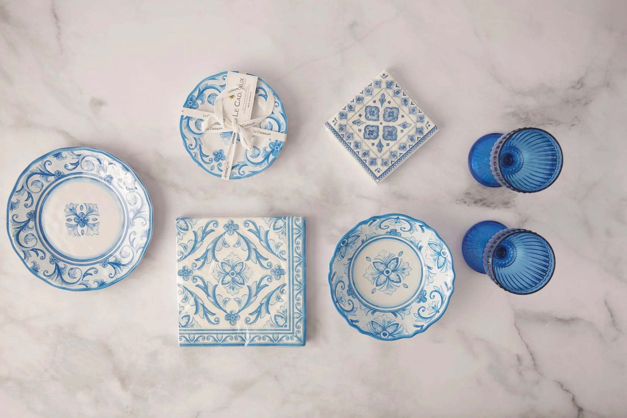 Blue and white tableware, napkins, and glassware styled together on a marble surface.