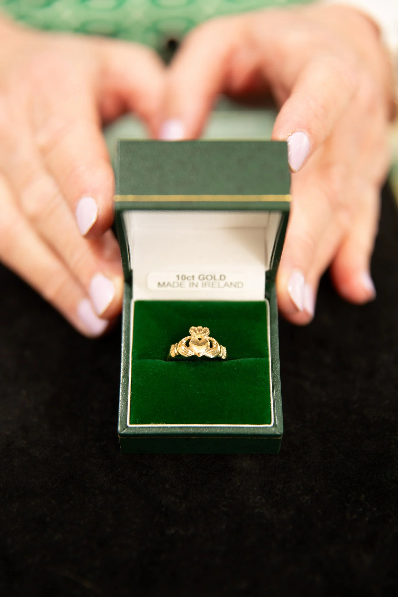 Hands presenting a green jewelry box with a gold Irish ring at The Irish Shop in Skippack, Pennsylvania.