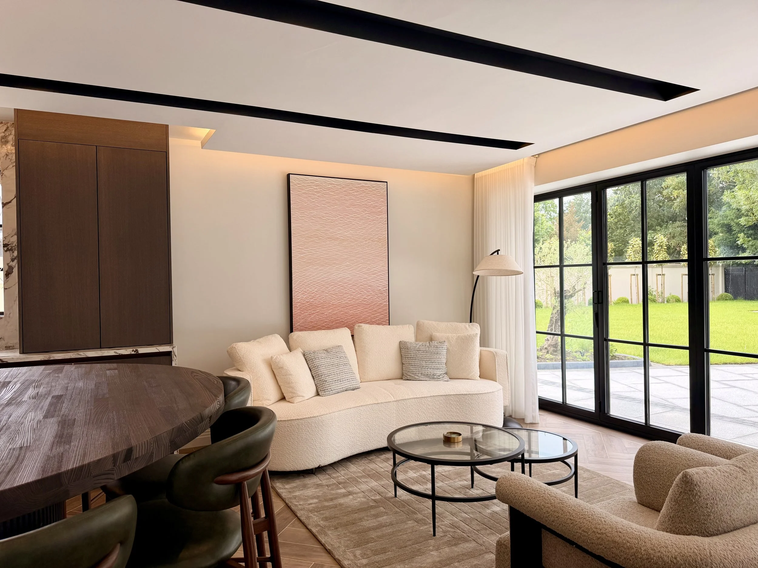 A sophisticated open-plan living area featuring architectural glazing, bespoke furniture, curated finishes and warm ambient lighting. Soft textures, contemporary furnishings and a carefully balanced palette create an inviting family space that seamle