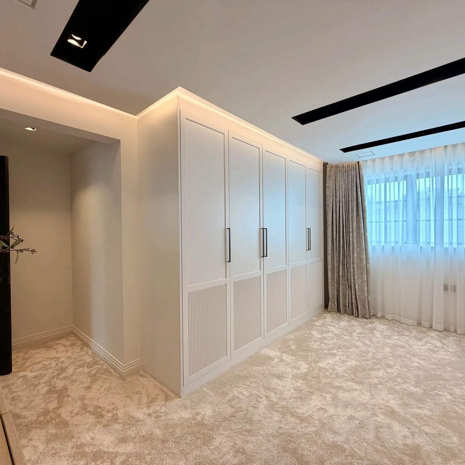 Custom fitted wardrobes with arched panel detailing and fluted lower panels in a luxury bedroom, designed and handcrafted by RK Studio