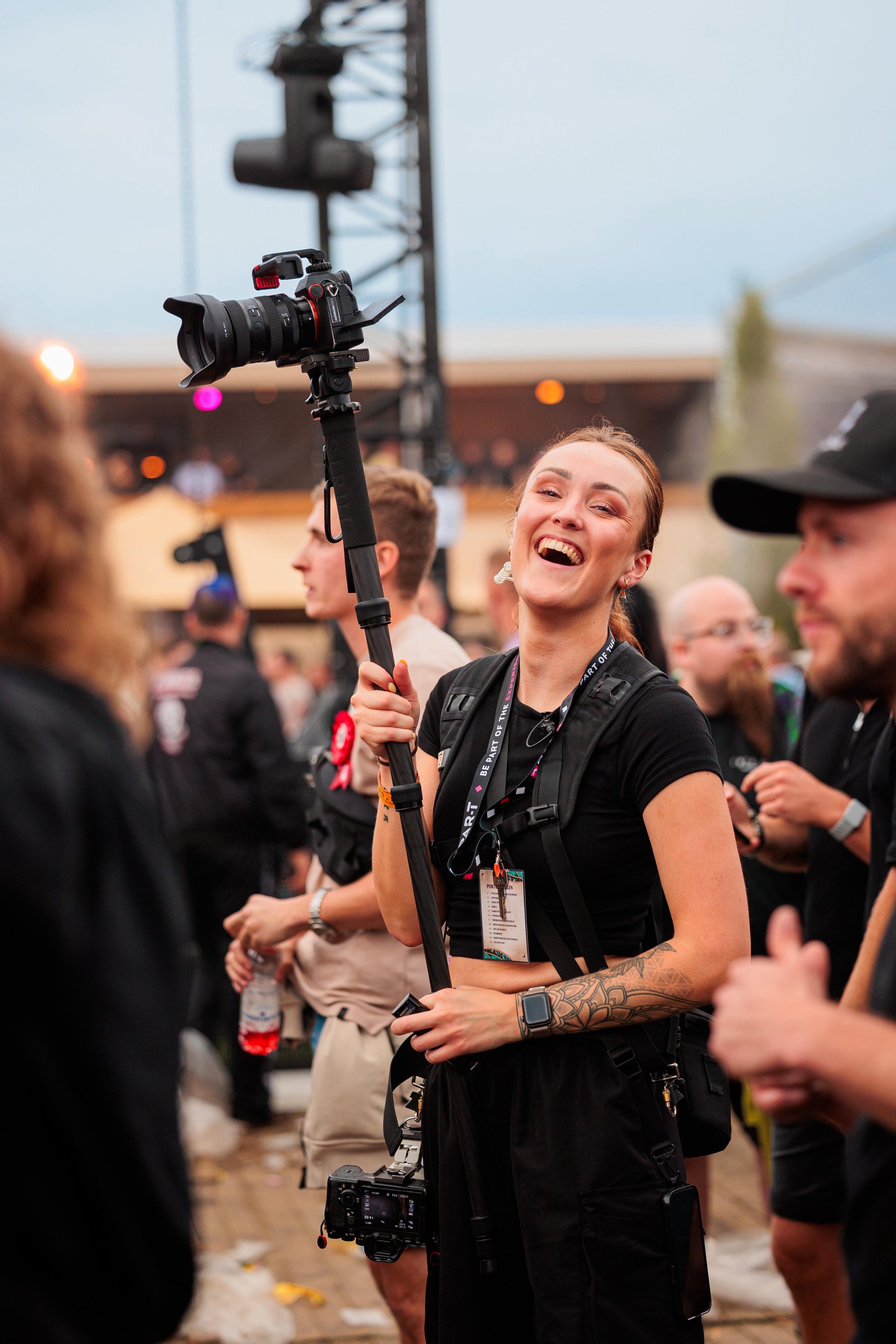 Vrouw met een camera op een statief, lachend aan het werk tijdens een evenement.