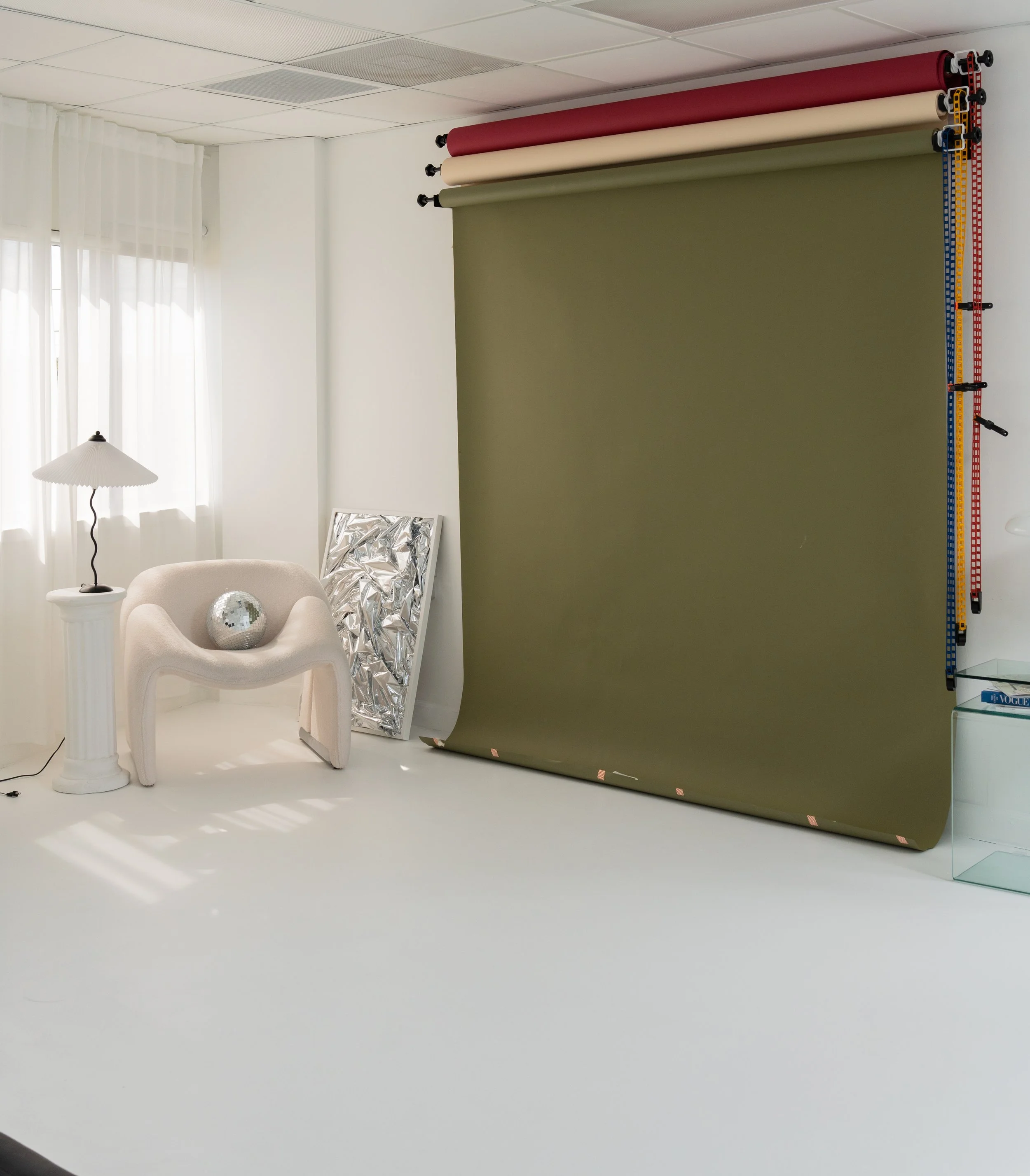Photography studio with a green backdrop, rolls of colored paper, and photography equipment, including a chair with a disco ball and a small lamp.