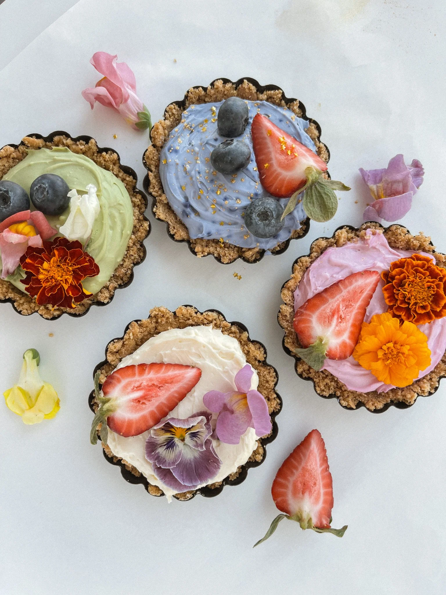 mini cheesecakes in green, blue, pink, and original decorated with flowers and fruits