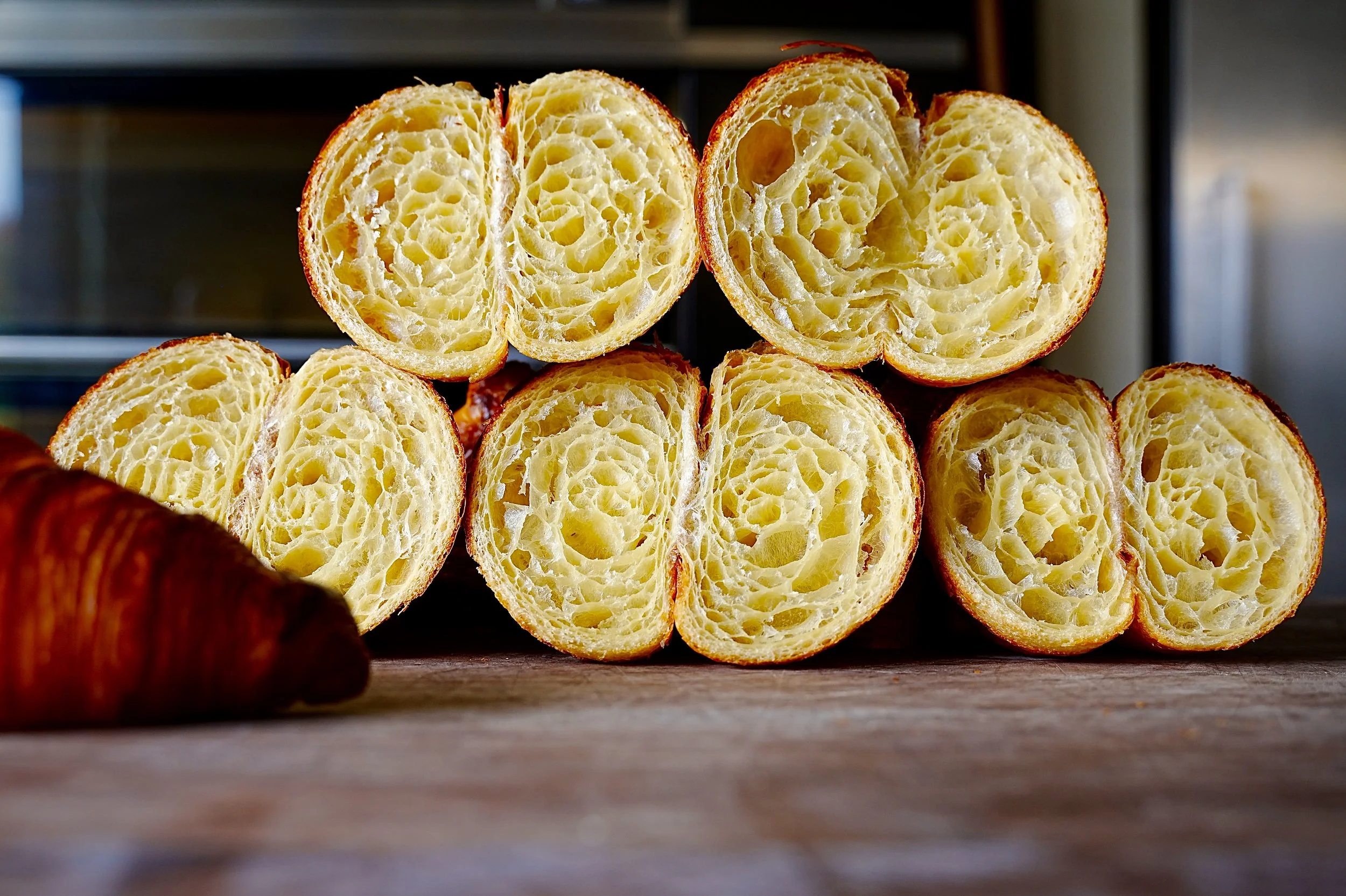 a pile of beautiful open crumbed croissants on a table in front of a deck oven
