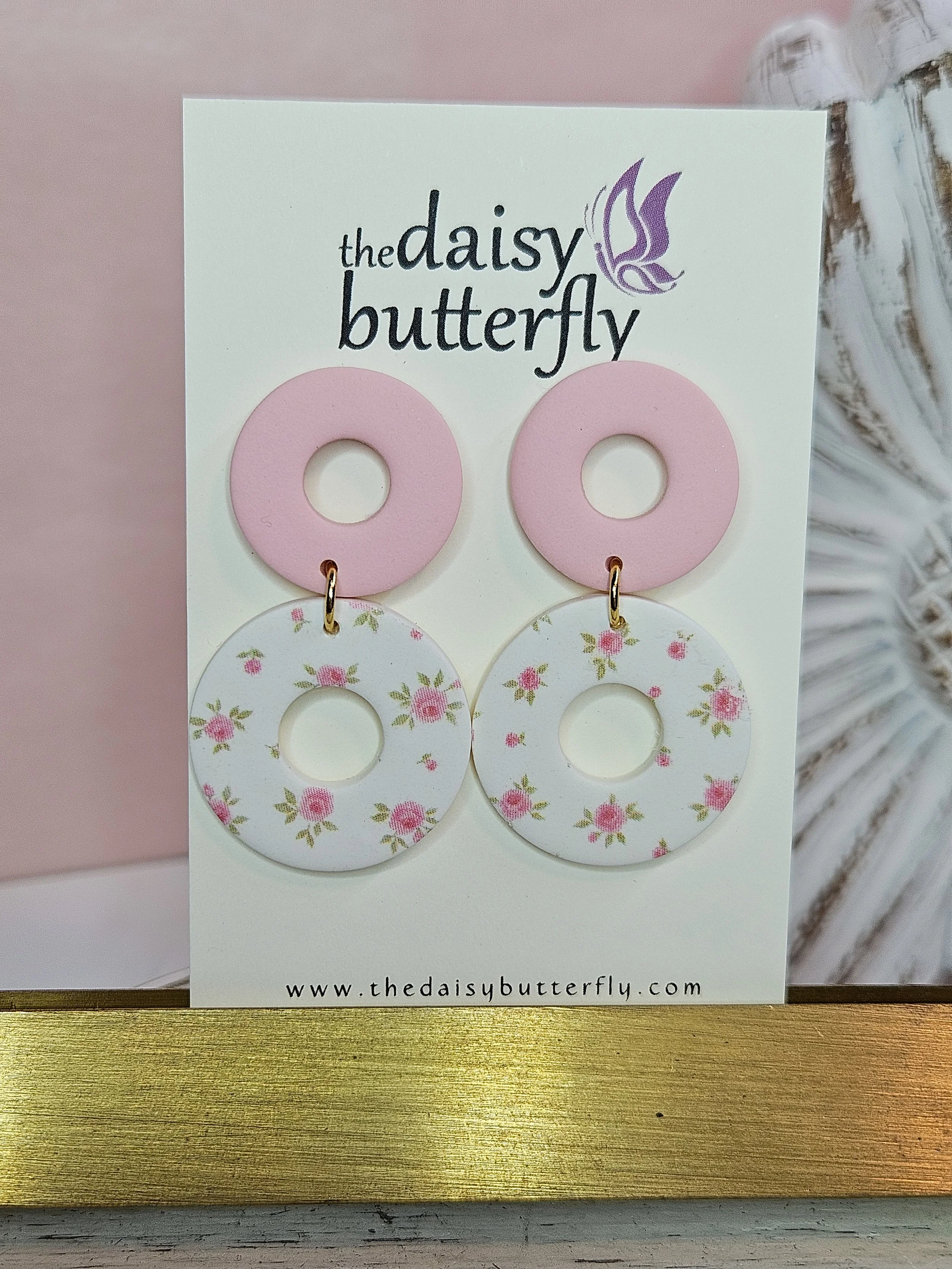 Pair of earrings with pink circular top and white circular bottom with pink floral pattern, displayed on a card from The Daisy Butterfly.