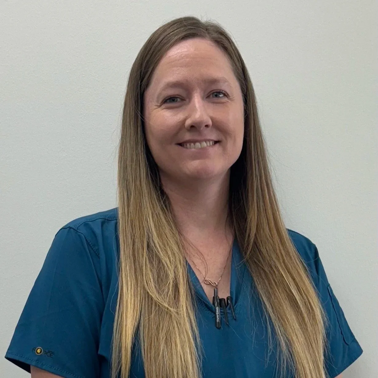 Nikki Thompson wearing a blue scrub top, smiling against a light background.