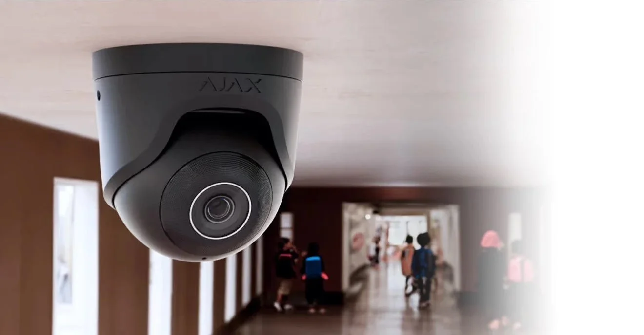 Security camera mounted on the ceiling inside a building with people walking in the background.
