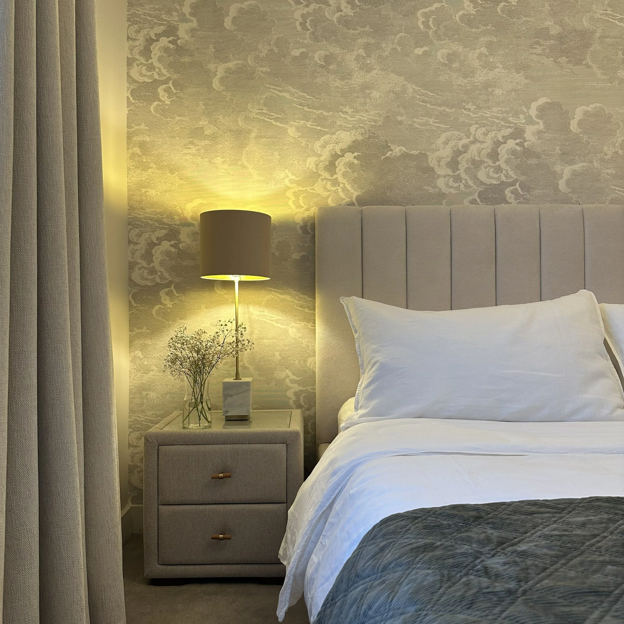 Modern calm bedroom interior design with upholstered headboard, textured wallpaper and soft bedside lighting.