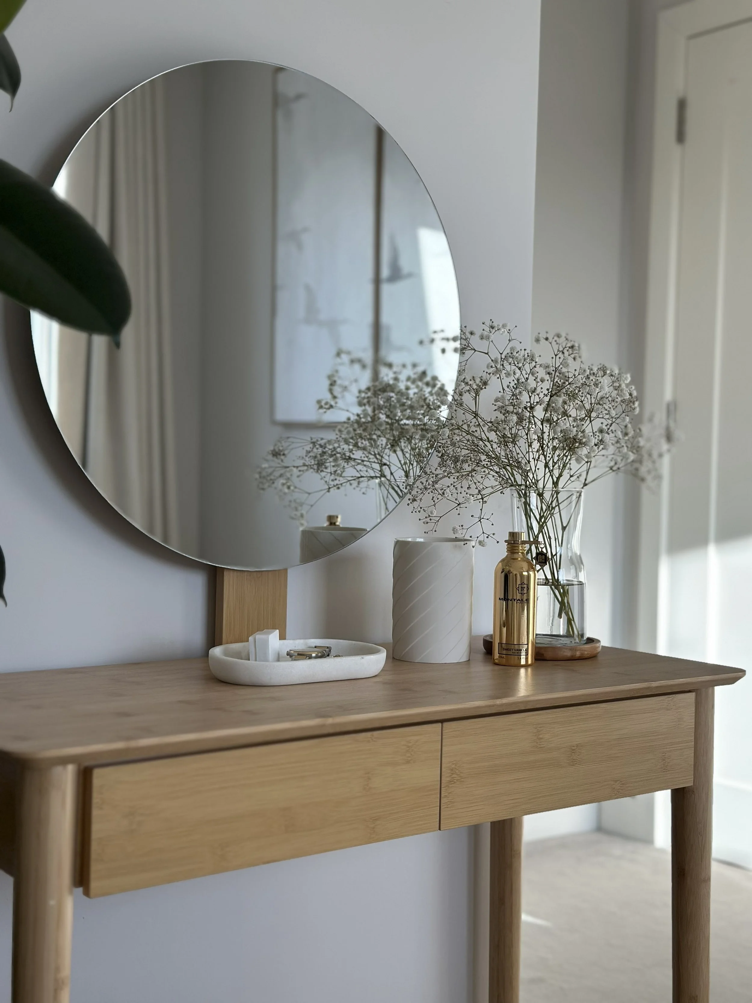 Minimal bedroom styling with natural wood console table, round mirror and decorative accessories.