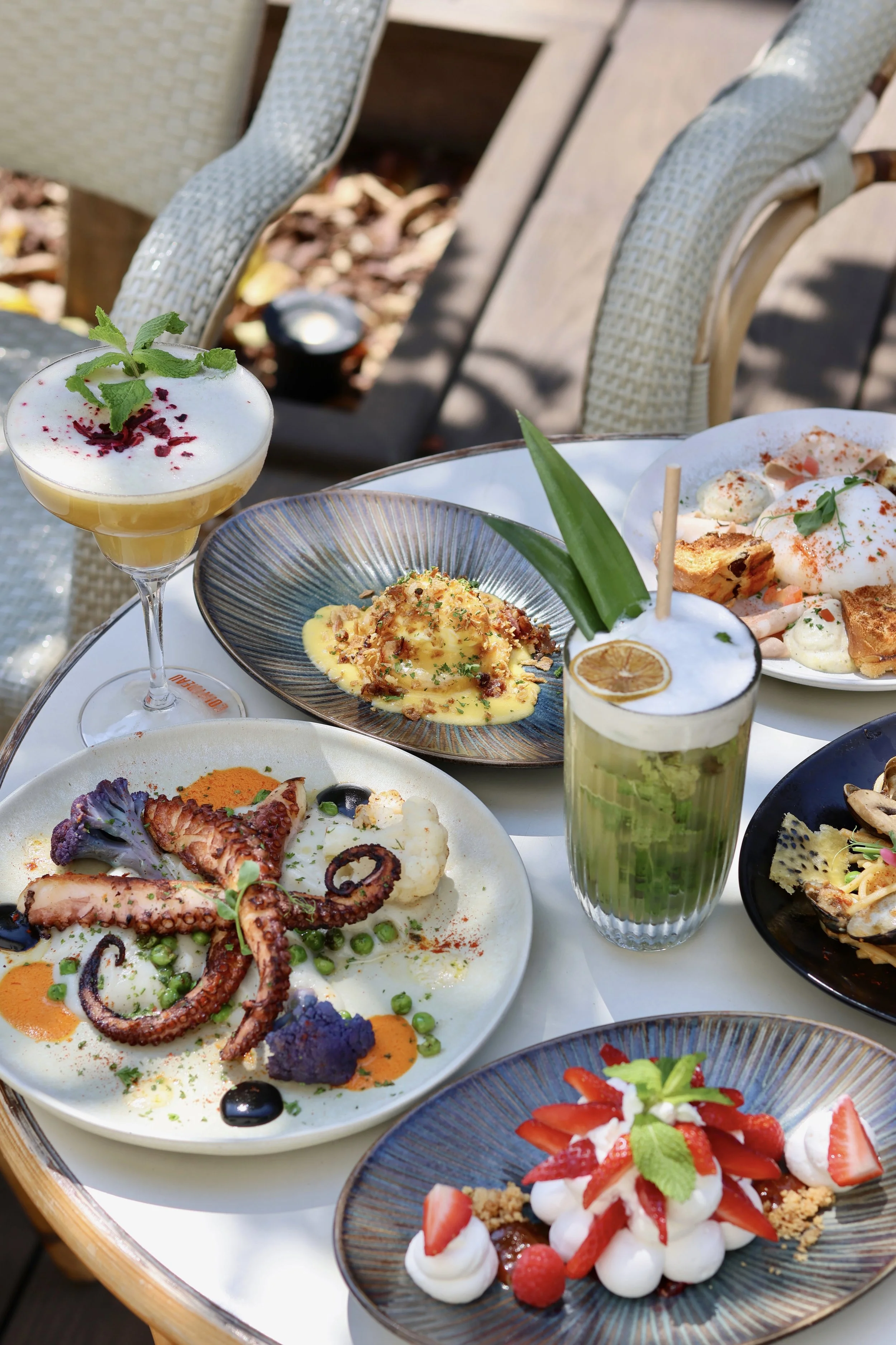 Assortiment de plats et desserts gastronomiques sur une table en extérieur, avec des boissons et de la vaisselle élégante.