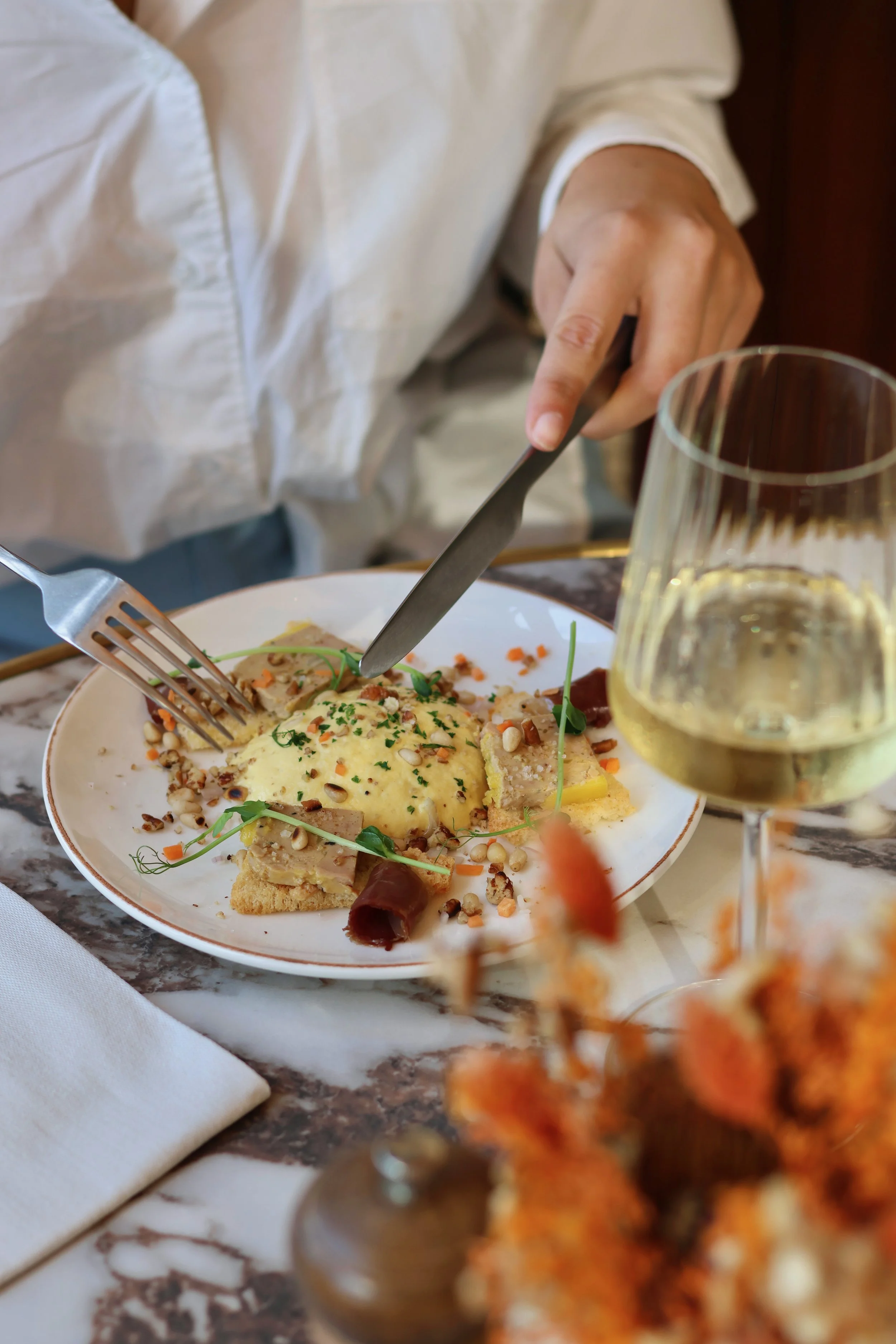 Person en haut blanc buccolique mangeant un plat avec un verre de vin blanc.