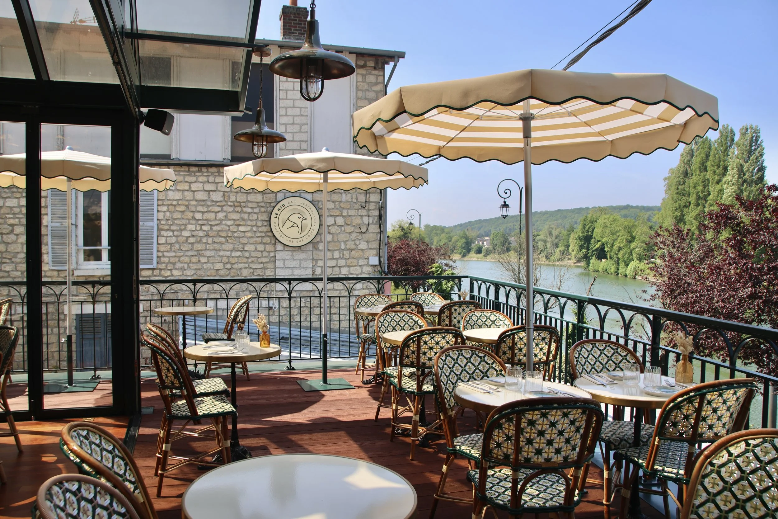  Terrasse de restaurant avec parasols, tables, chaises, vue sur la rivière et la nature environnante.