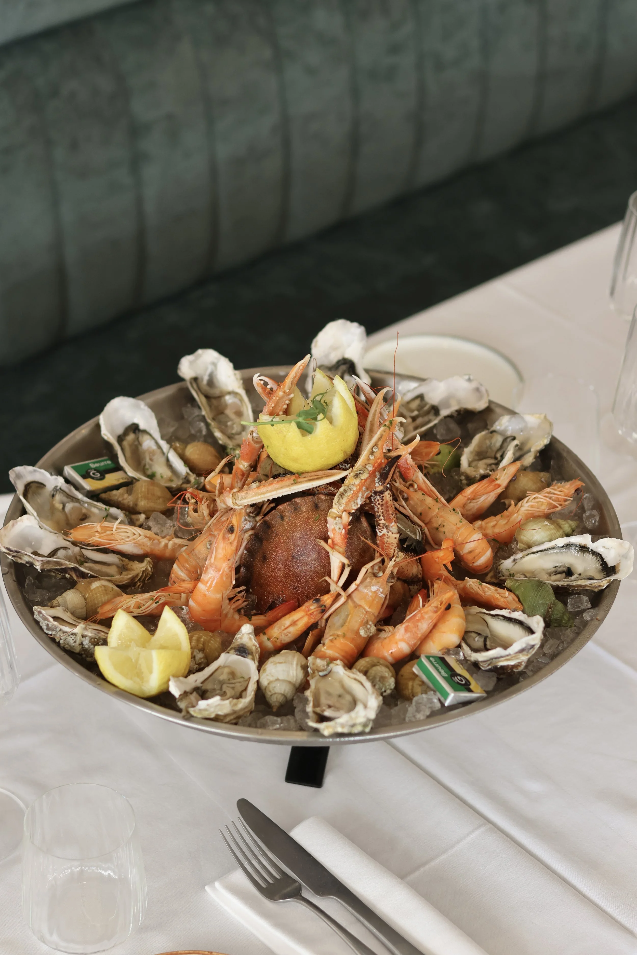 Plate de fruits de mer avec huîtres, crevettes, un homard, citron et autres coquillages sur glace sur une table.