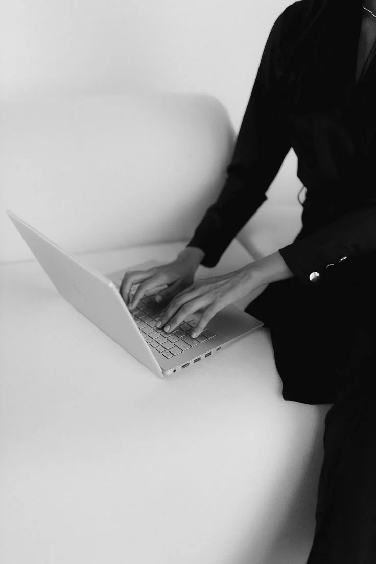 Person in black clothing working on a laptop computer on a white table.