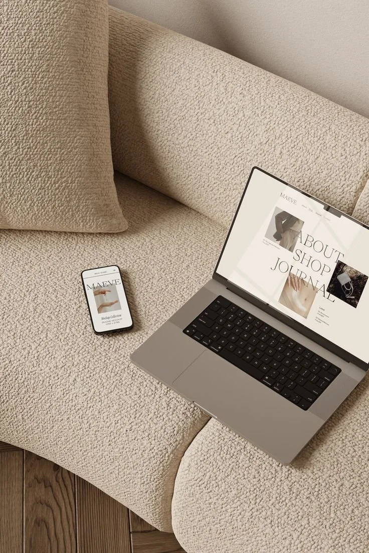 Laptop and smartphone on a beige textured couch with a beige pillow and wooden floor