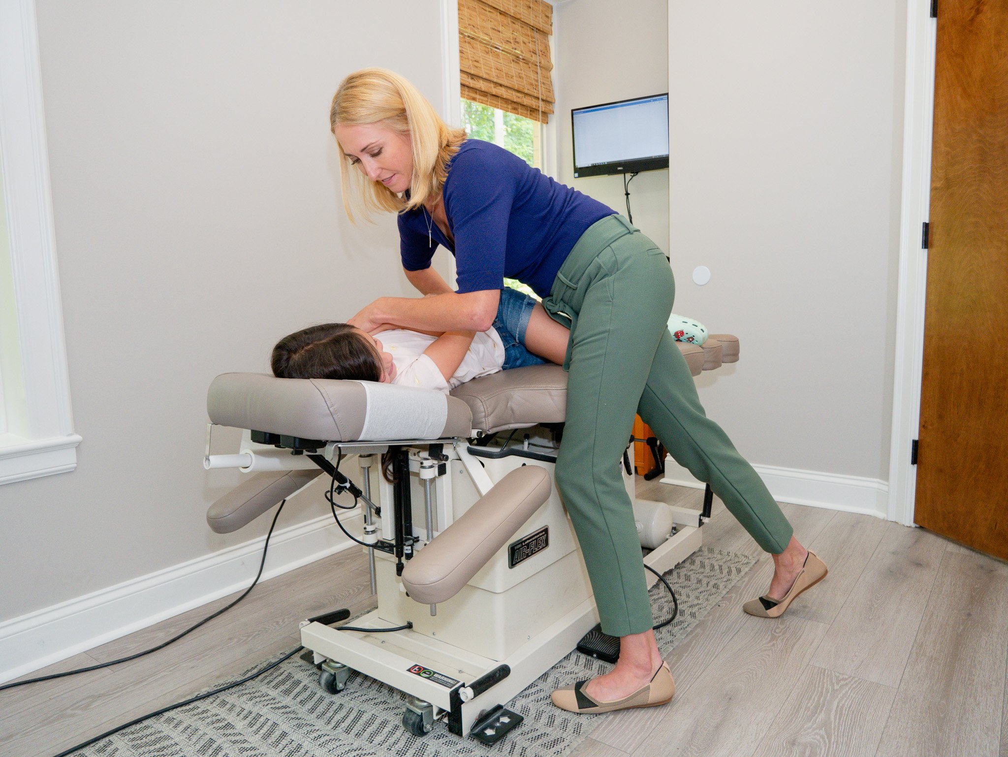 A chiropractor adjusting a patient's back on an adjustment table in a clinic room.