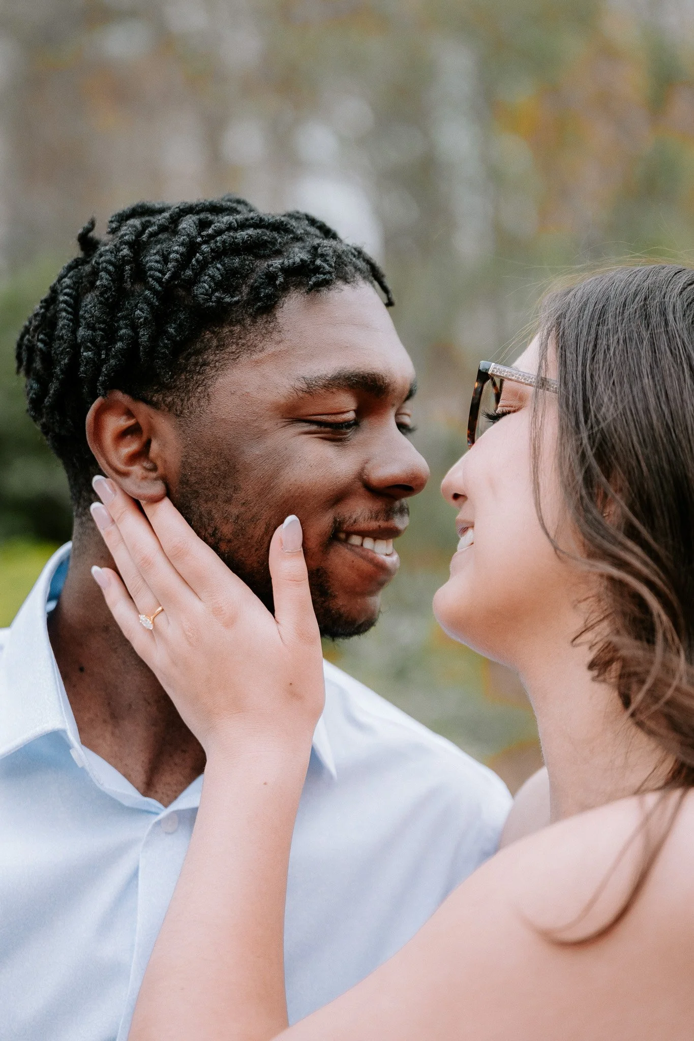 A couple smiling at each other closely. The woman has her hand on the man's cheek, wearing an engagement ring. Charlotte NC Couples Engagement Portrait Photoshoot