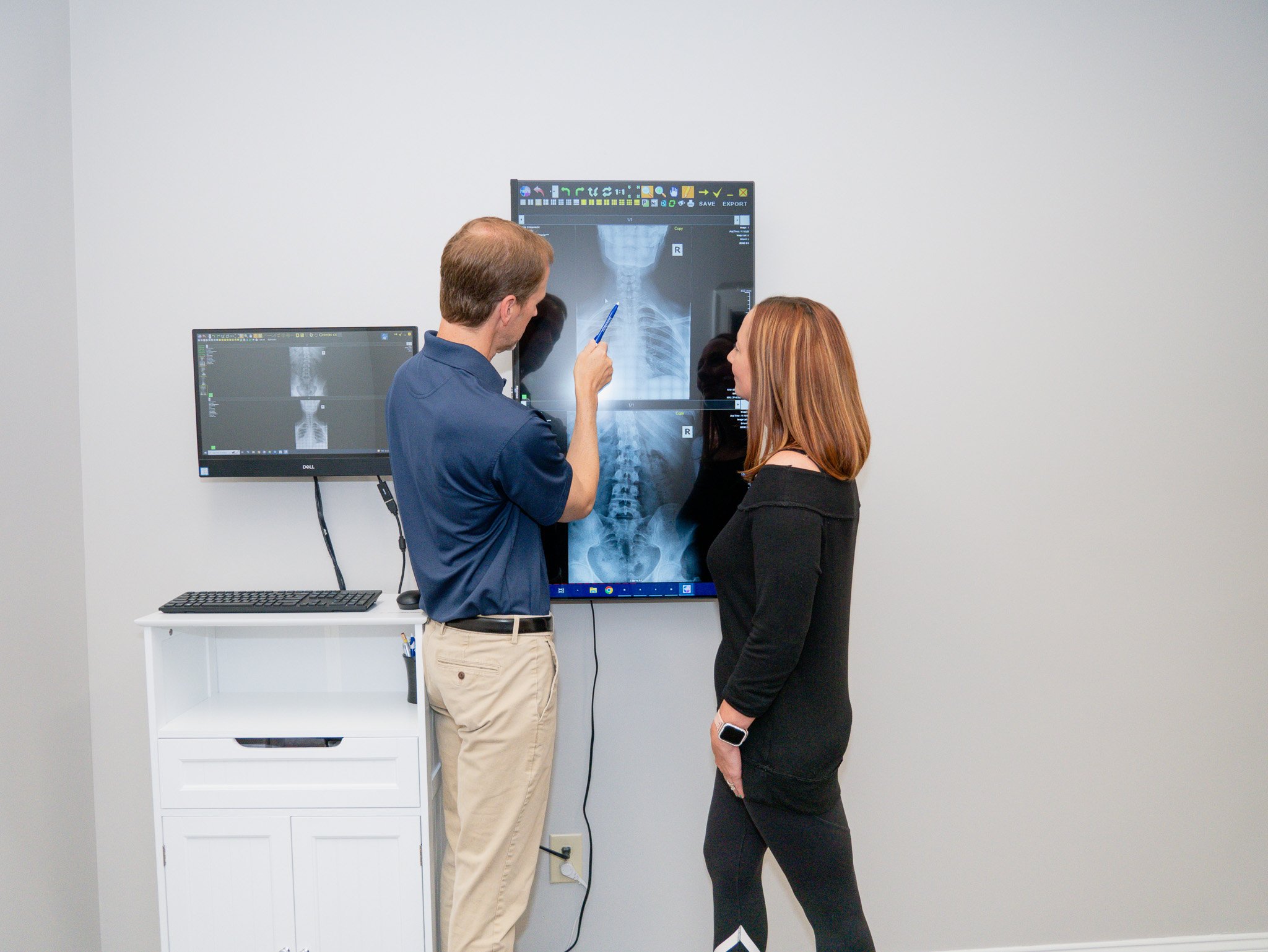 Doctor and patient reviewing spine X-rays on a screen in a medical office.