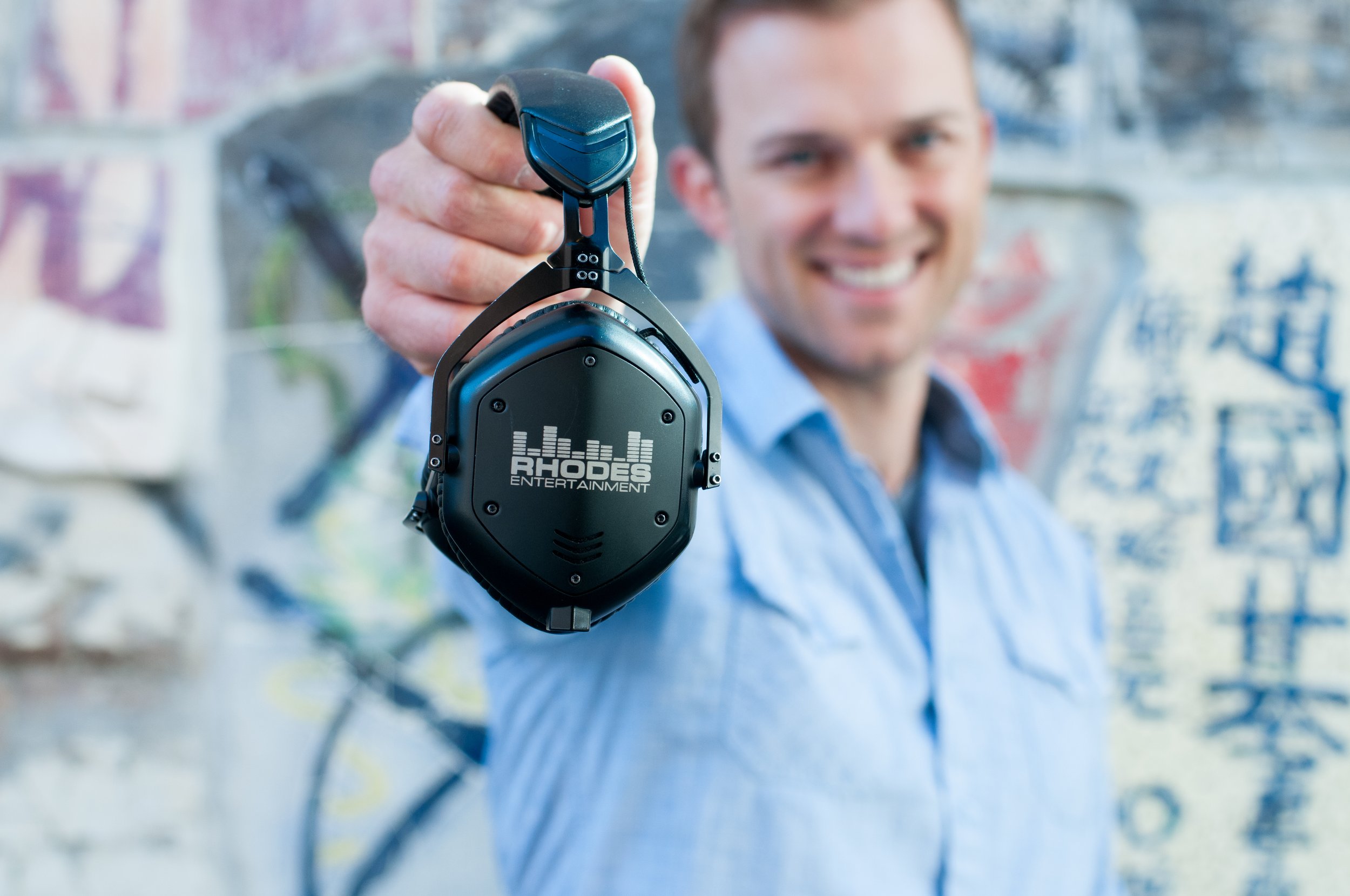 Man in blue buttondown holding a pair of headphones out toward the lens of the camera