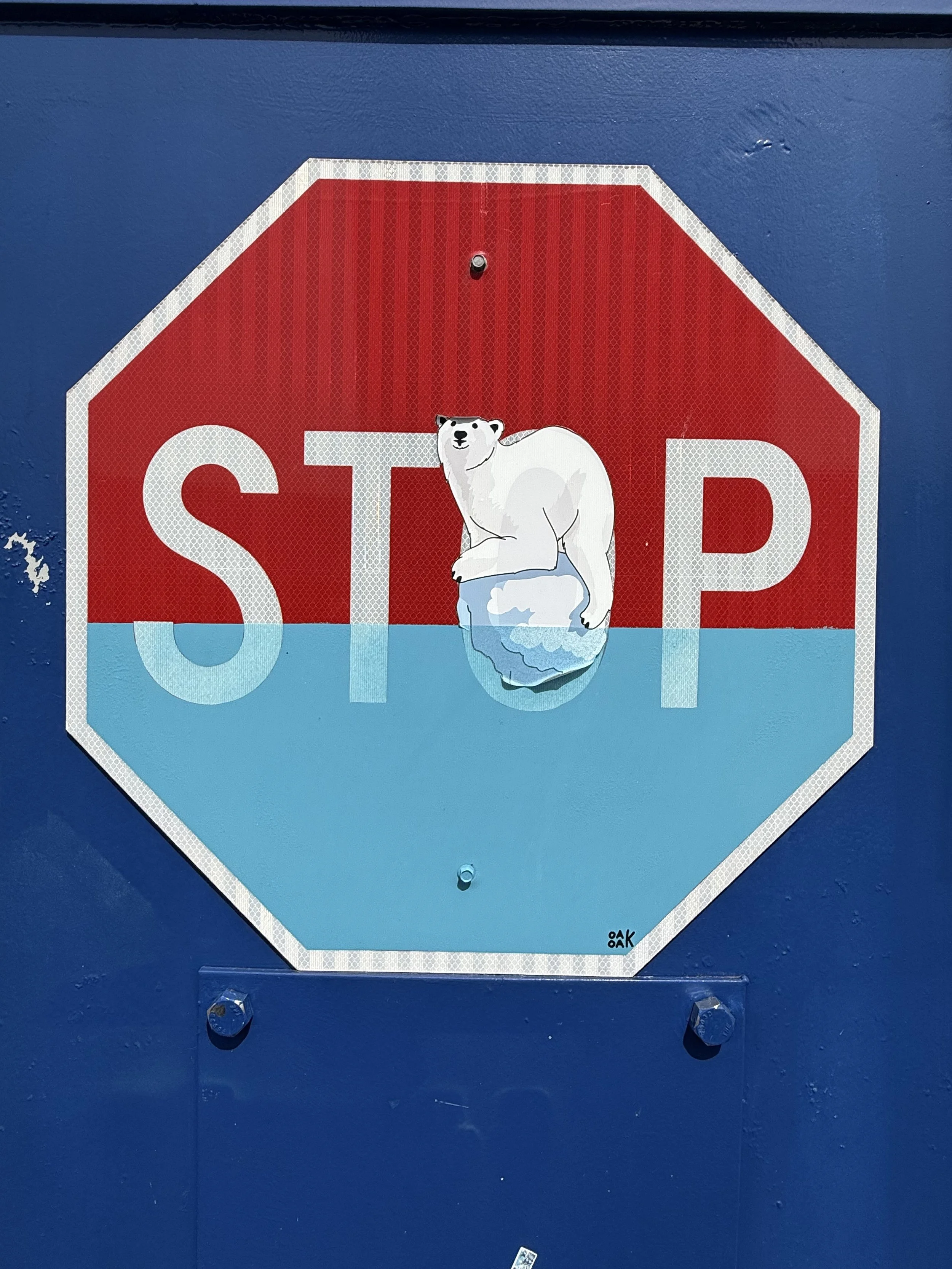 A stop sign with a polar bear sticker at the bottom, with the bear sitting on an iceberg, on a blue wall.