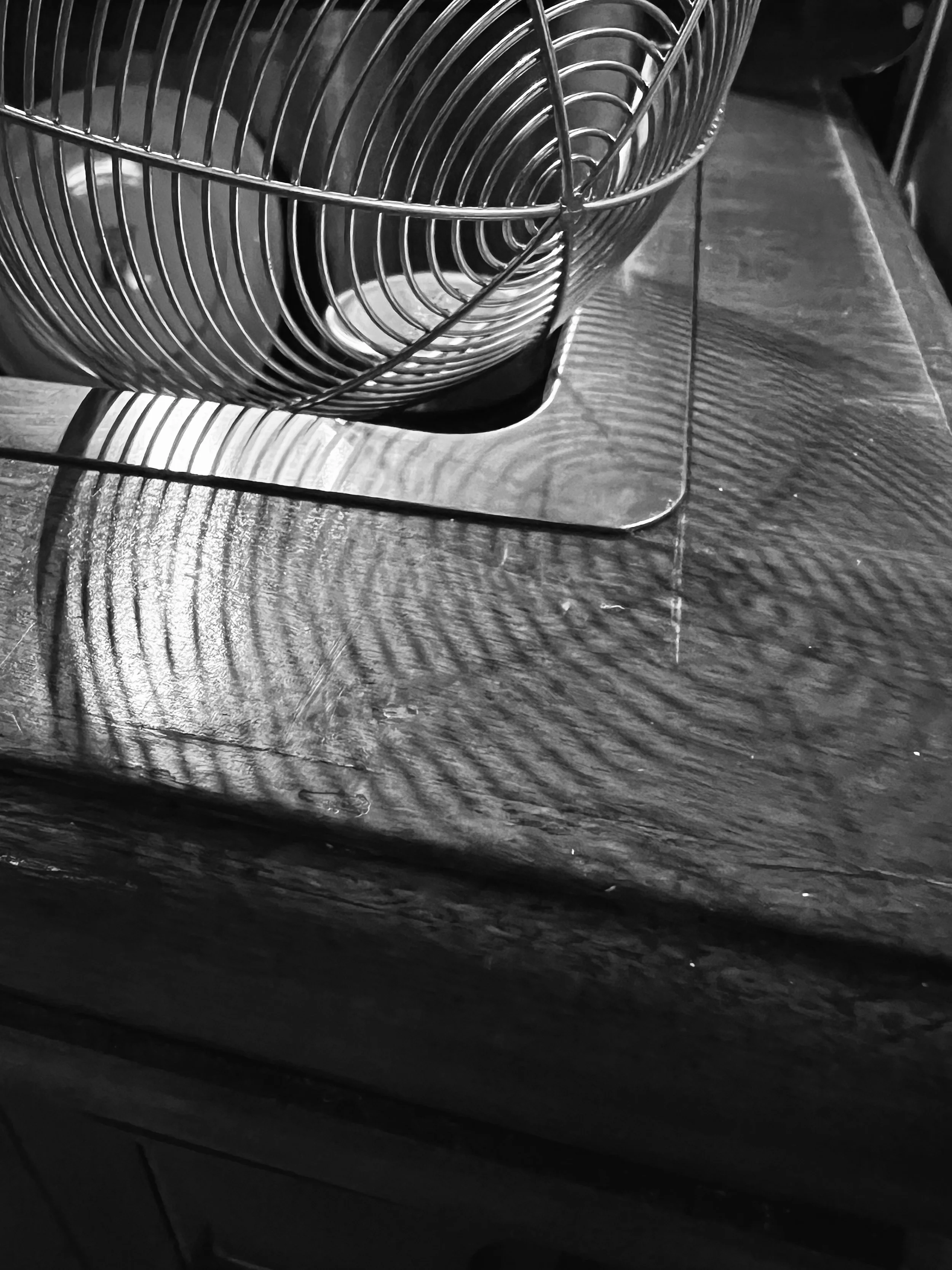 Black and white photo of a metal dish drying rack with a glass underneath on a wooden surface.