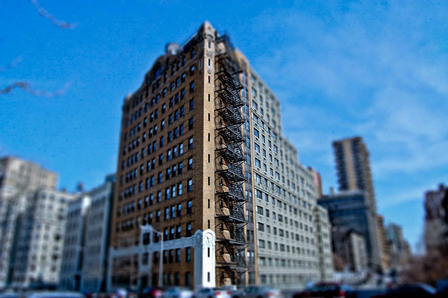 Tall urban building with fire escape ladders on its facade, surrounded by other high-rise buildings under a clear blue sky.