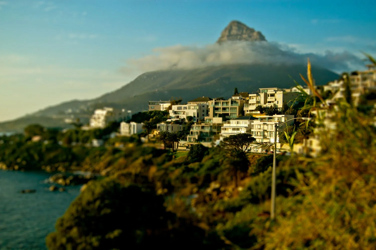 Hilly coastal neighborhood with modern white buildings and Mount Kilimanjaro in the background, partly obscured by clouds.