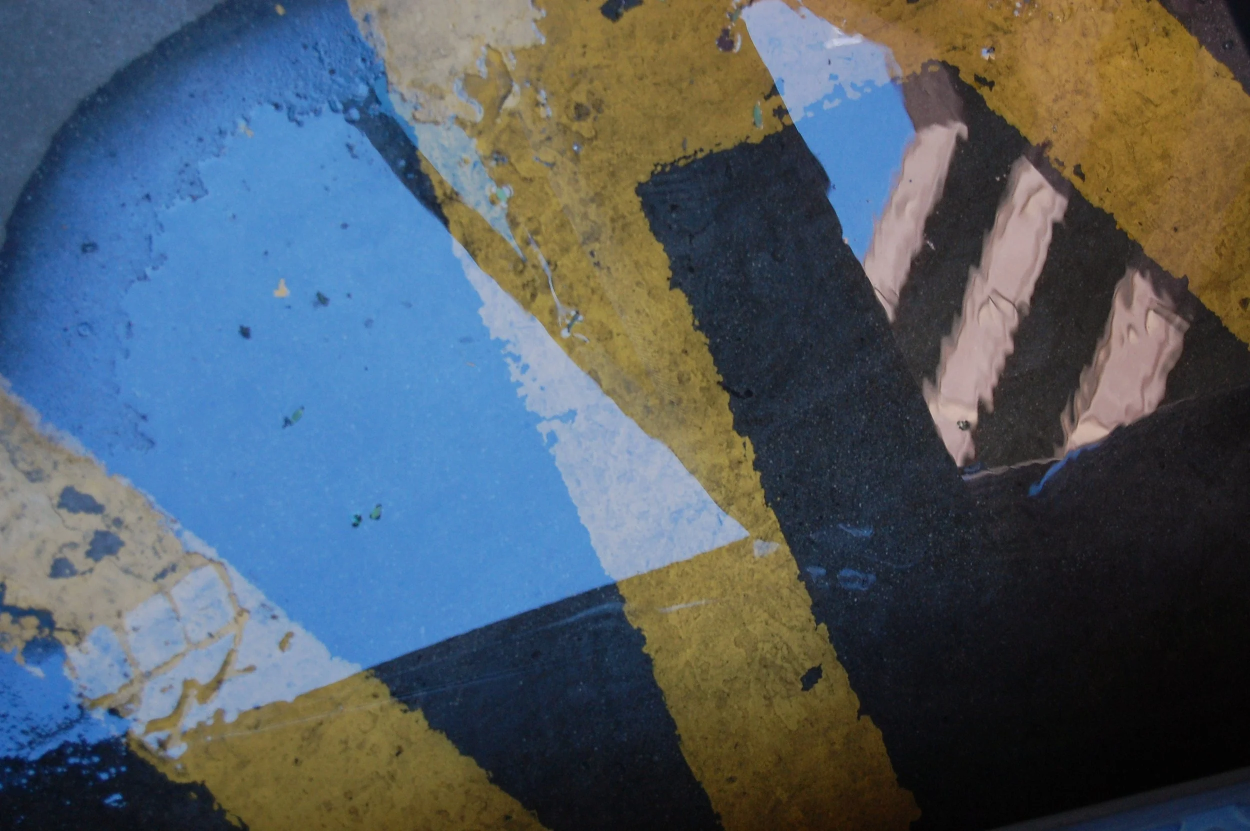 Close-up of a painted street surface with yellow, black, and blue markings, showing chipped and worn paint.