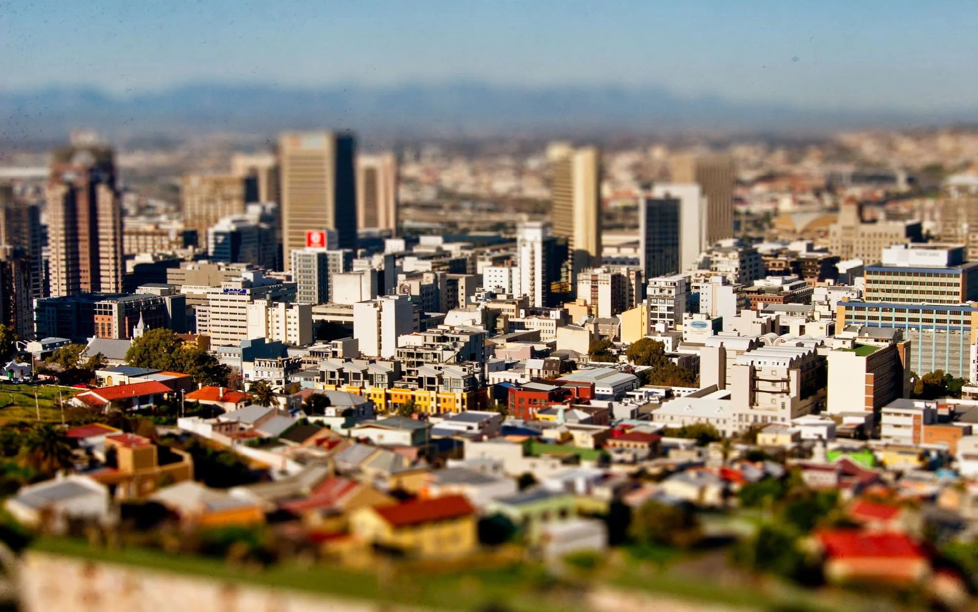 A city skyline with high-rise buildings and residential houses in the foreground, under a clear sky.
