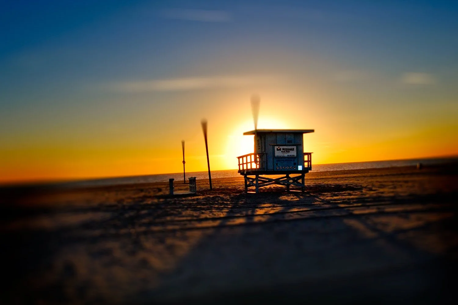 Beach scene during sunset with a lifeguard tower, two wind socks, and a sandy beach.