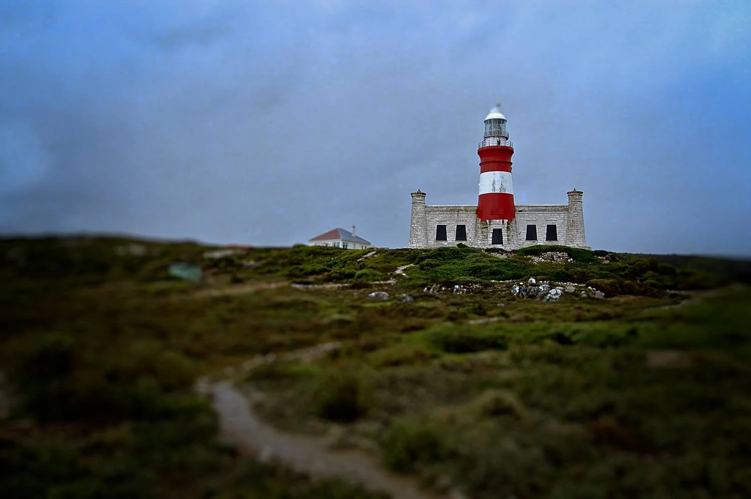 Lighthouse on a grassy hill with a cloudy sky in the background.