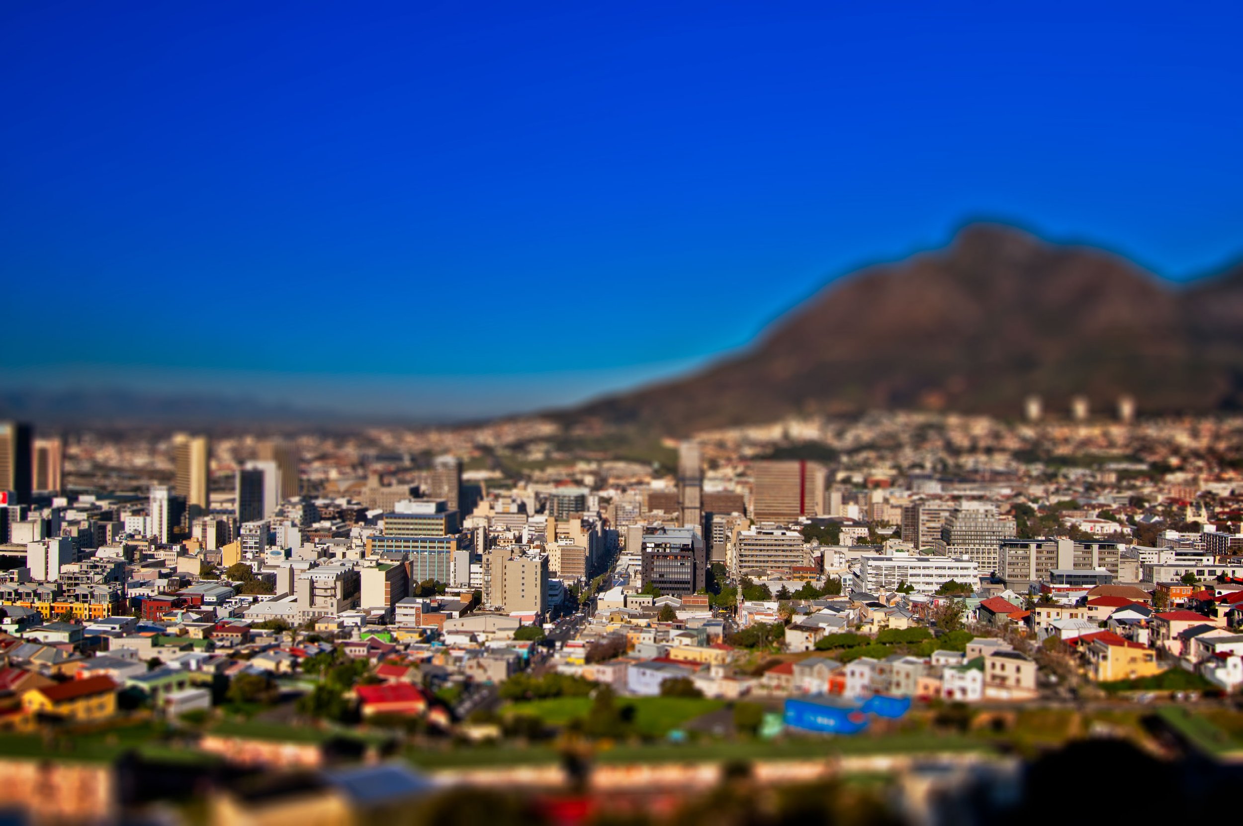 A cityscape with numerous buildings in the foreground and a mountain in the background under a clear blue sky.