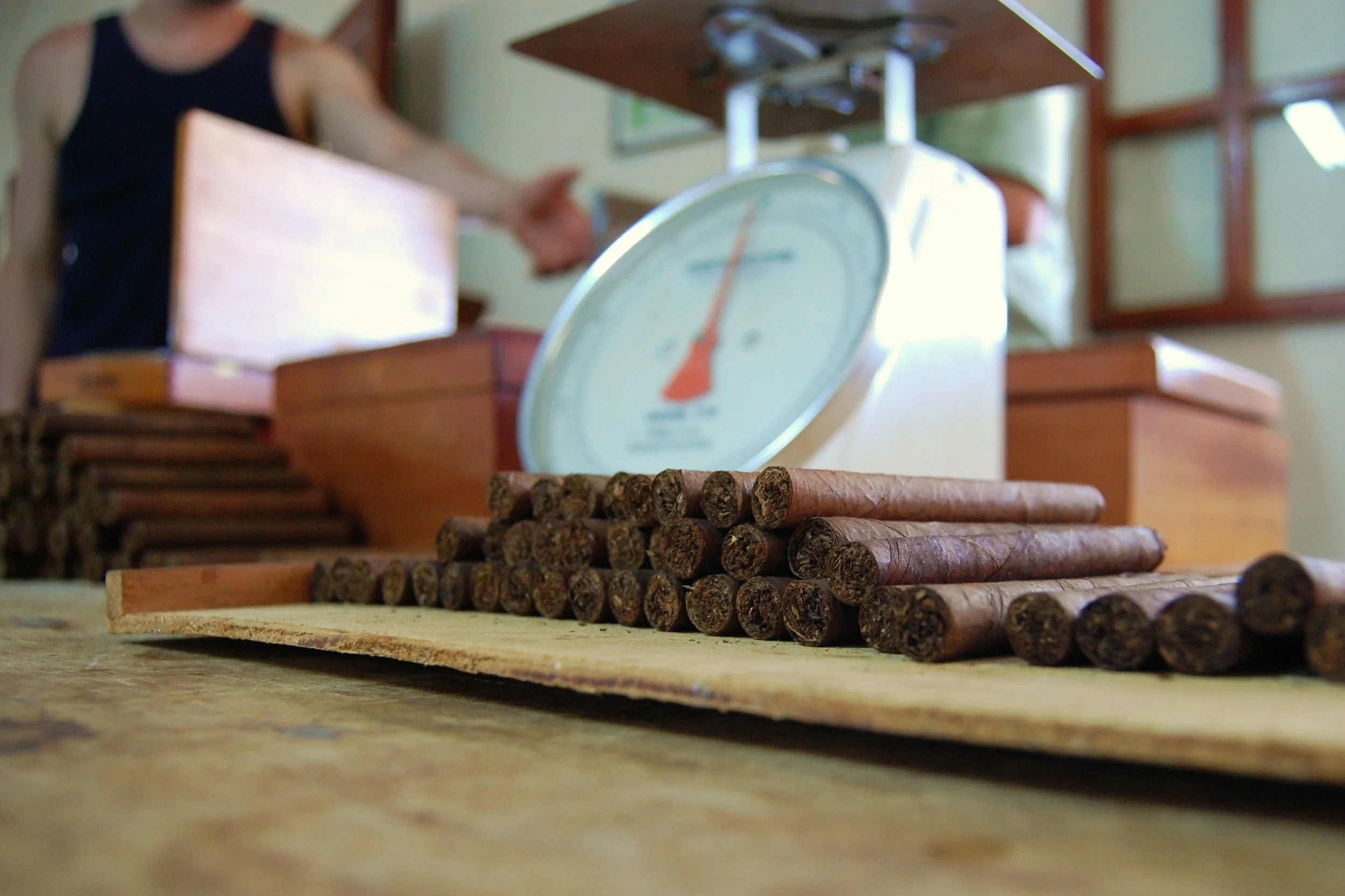 A stack of cigars on a wooden surface with a vintage scale in the background.