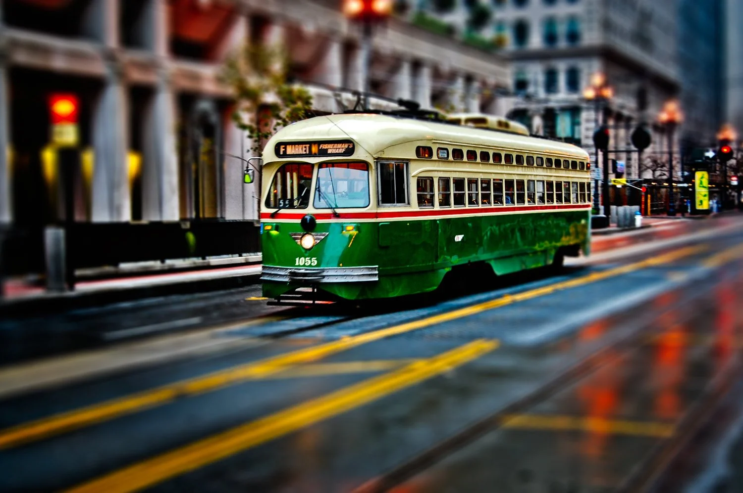 A vintage green and cream trolley car with the number 1055 on a city street, displaying the route 'F Market / Fisherman's Wharf'.