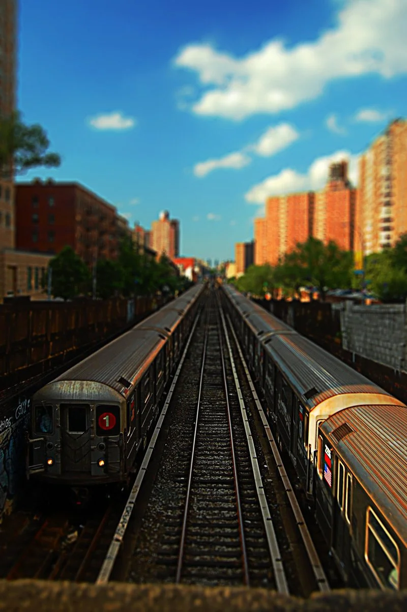 Subway train on elevated tracks in an urban area with tall buildings and a blue sky with clouds.