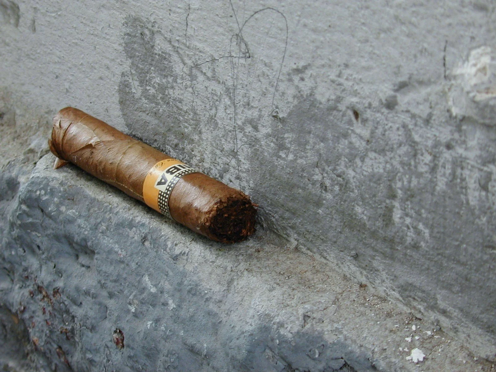 A used cigar resting on a weathered concrete surface next to a concrete wall.
