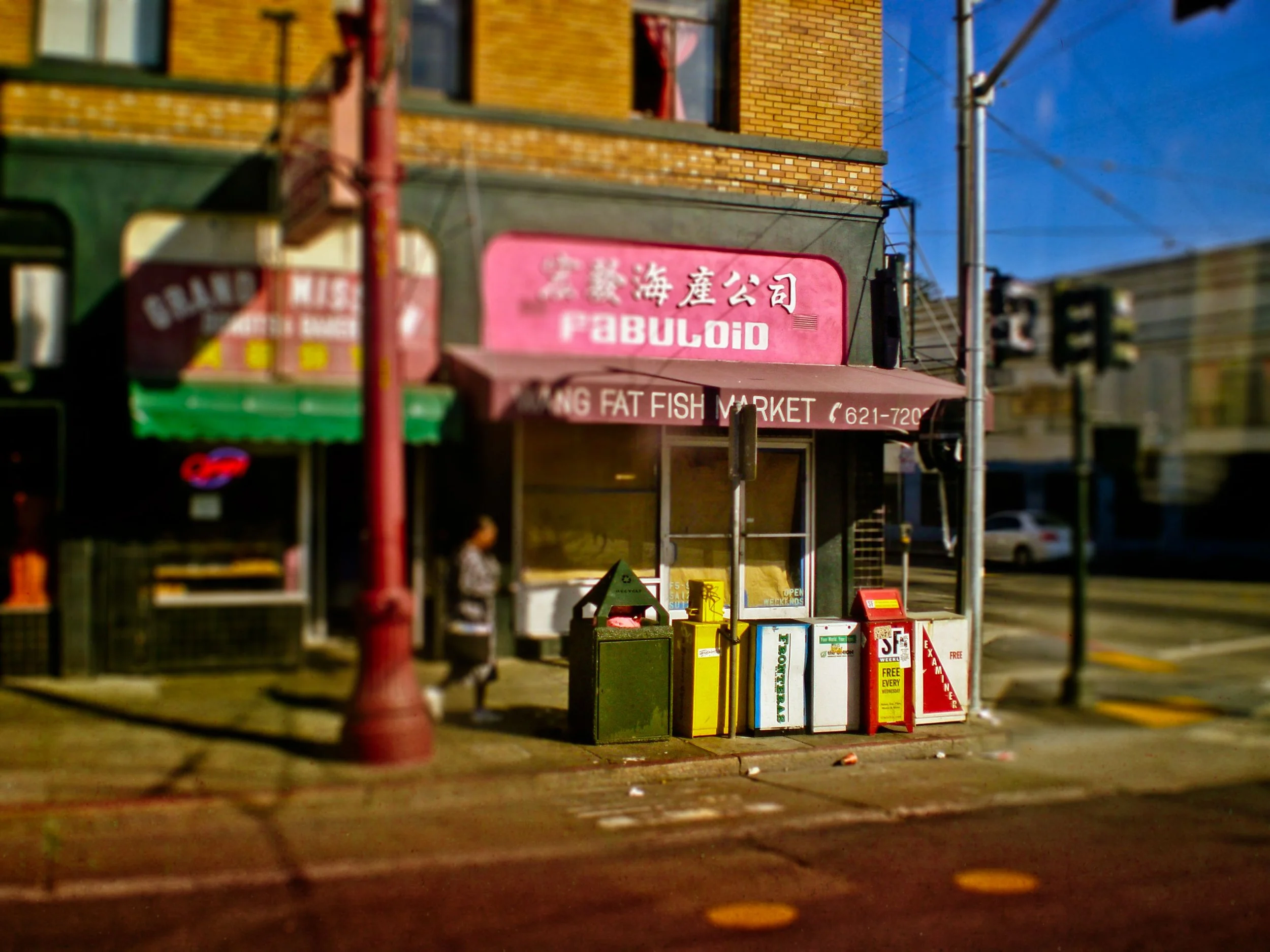 Storefront with pink sign reading 'FabuloiD' in Chinese characters, newspaper racks, and a person on the sidewalk, with utility pole and power lines overhead.