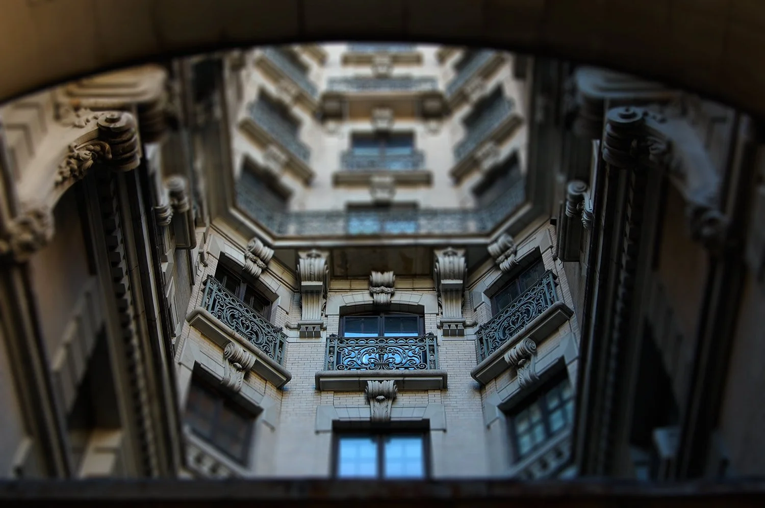 View of a multi-story building's interior courtyard from the bottom, showing decorative balconies and ornate architectural details.