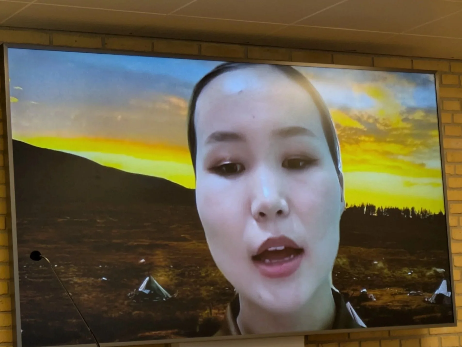 The photo shows Dukha herder Khongorzul on a video call in front of a photo of tipis